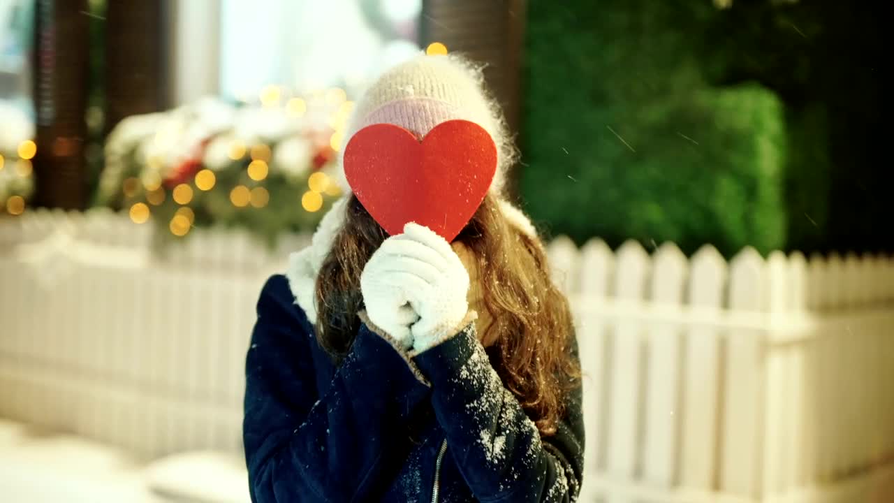 Free Video Stock Smiling Woman Covers Face With Heart Cutout In Snowy Street Live Wallpaper - Free Download