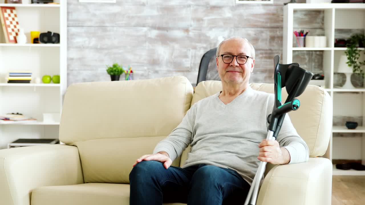 Free Video Stock Smiling Elderly Man Holding Crutches And Sitting On Sofa Live Wallpaper - Free Download